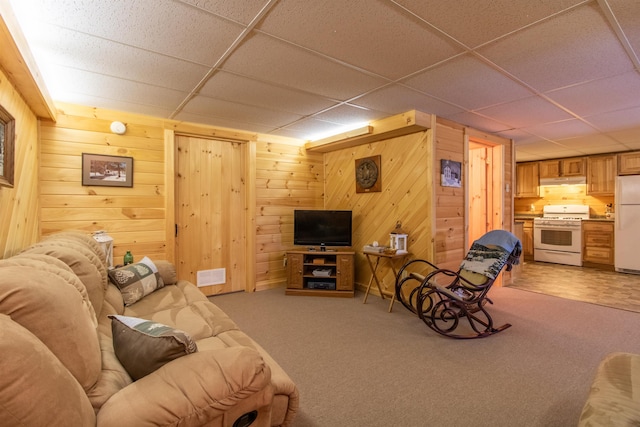 living room featuring carpet floors, a paneled ceiling, and wood walls