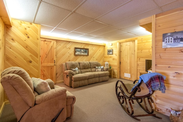 living room with a drop ceiling, wooden walls, and carpet