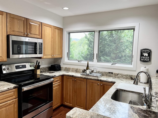 kitchen with stainless steel appliances, light stone countertops, sink, and dark hardwood / wood-style flooring