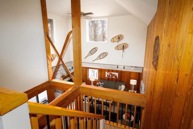 staircase with vaulted ceiling, ceiling fan, and wood walls