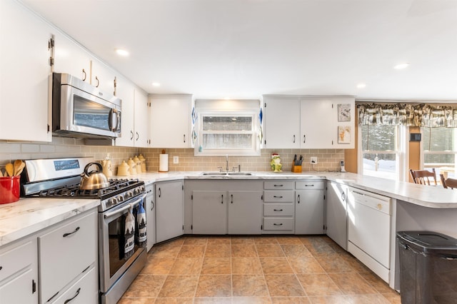 kitchen with sink, appliances with stainless steel finishes, gray cabinetry, backsplash, and white cabinets