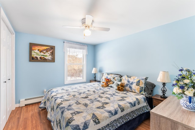 bedroom with a baseboard heating unit, hardwood / wood-style floors, ceiling fan, and a closet