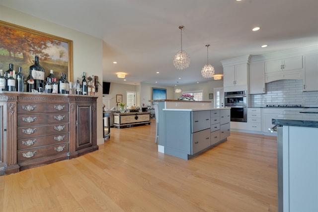 kitchen featuring pendant lighting, white cabinetry, backsplash, light hardwood / wood-style floors, and stainless steel double oven