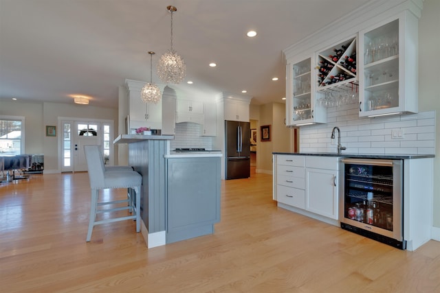 kitchen featuring wine cooler, black fridge, white cabinetry, hanging light fixtures, and light wood-type flooring