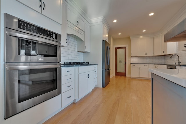 kitchen with tasteful backsplash, appliances with stainless steel finishes, light hardwood / wood-style flooring, and white cabinets