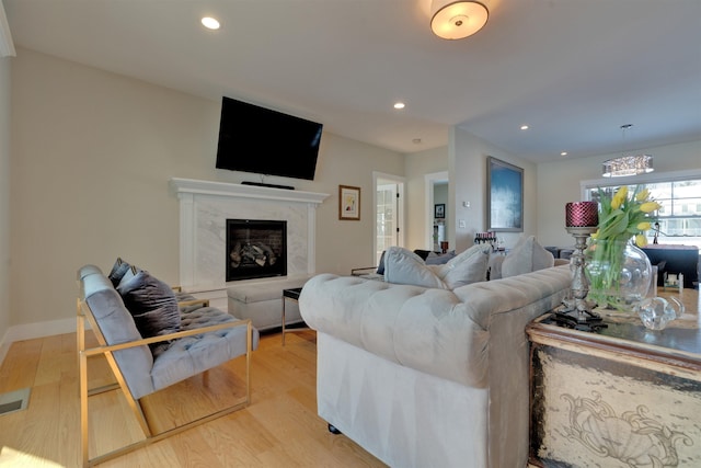 living room with a high end fireplace and light hardwood / wood-style flooring