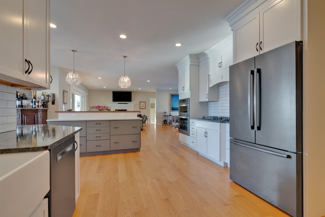 kitchen with pendant lighting, white cabinets, decorative backsplash, stainless steel appliances, and light wood-type flooring