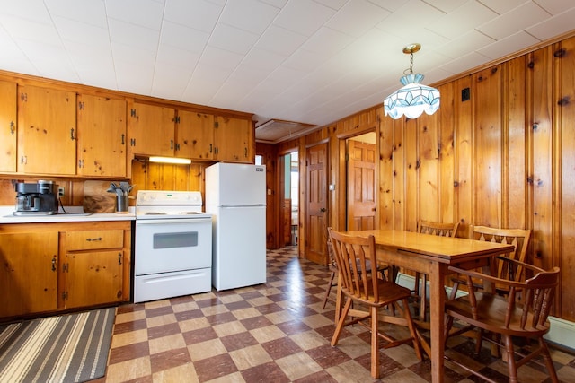 kitchen featuring white appliances, decorative light fixtures, and wood walls