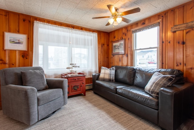 living room with light carpet, a baseboard heating unit, ceiling fan, and wood walls