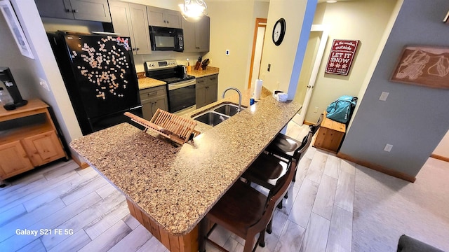 kitchen with sink, gray cabinetry, a kitchen breakfast bar, light stone countertops, and black appliances