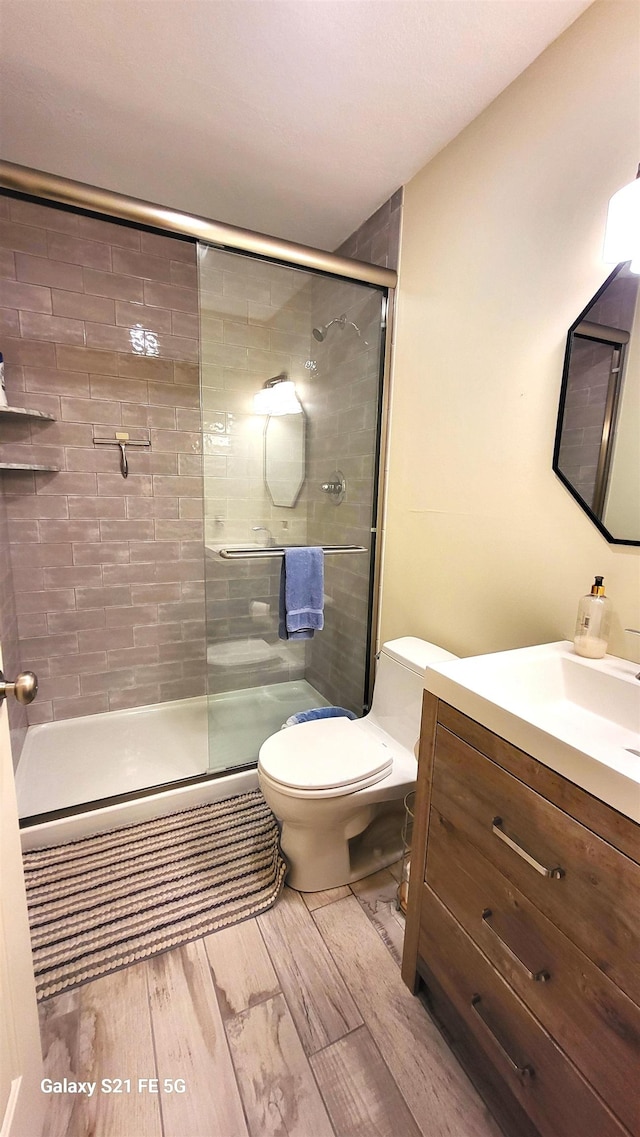 bathroom with hardwood / wood-style flooring, vanity, toilet, and a shower with shower door