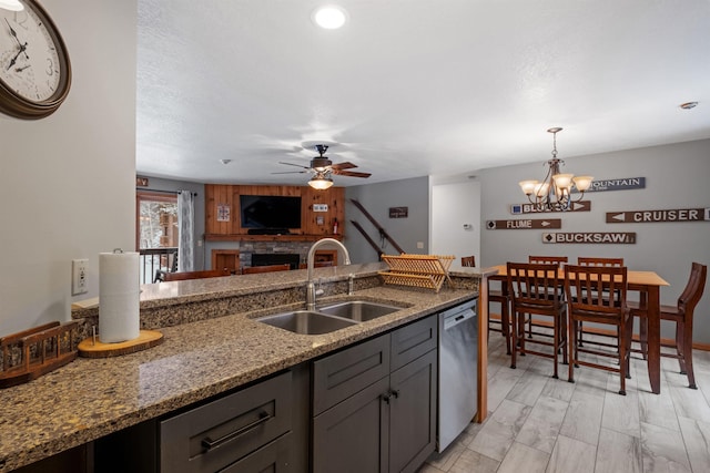 kitchen featuring pendant lighting, sink, light stone countertops, ceiling fan with notable chandelier, and stainless steel dishwasher