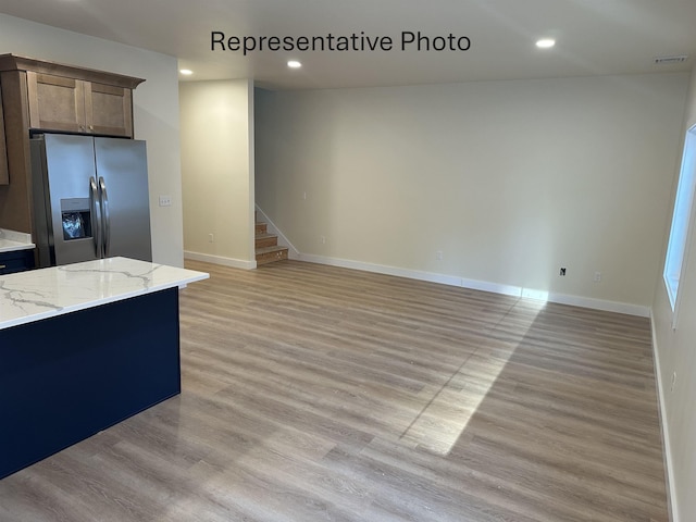 kitchen with light hardwood / wood-style flooring, stainless steel fridge, and light stone countertops