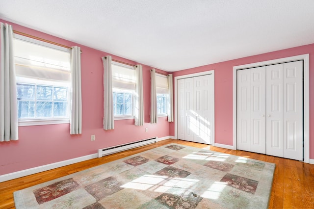 unfurnished bedroom with multiple closets, a baseboard radiator, and wood-type flooring