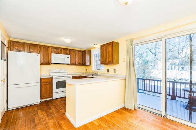 kitchen with white appliances, wood-type flooring, kitchen peninsula, and sink