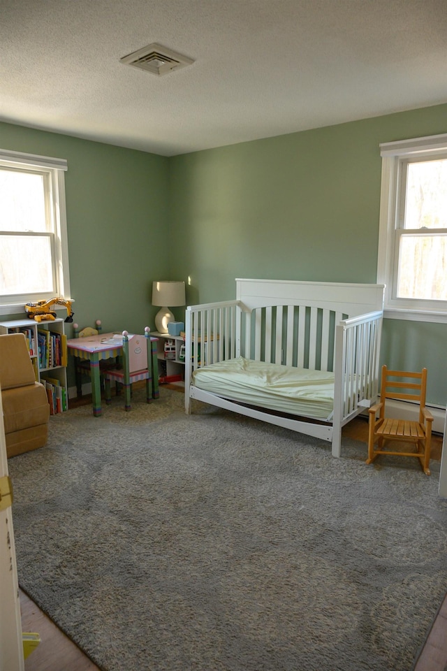 carpeted bedroom with multiple windows, a crib, and a textured ceiling