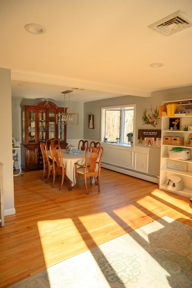 dining space featuring hardwood / wood-style flooring, a baseboard radiator, and a textured ceiling