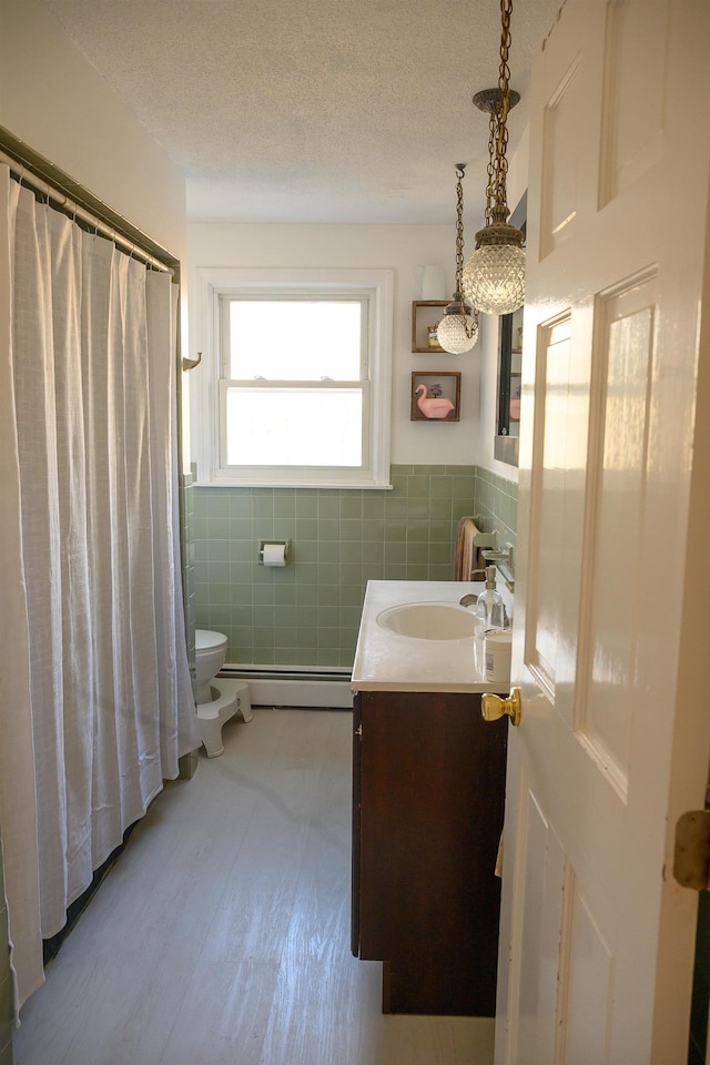 bathroom with a baseboard radiator, tile walls, vanity, toilet, and a textured ceiling