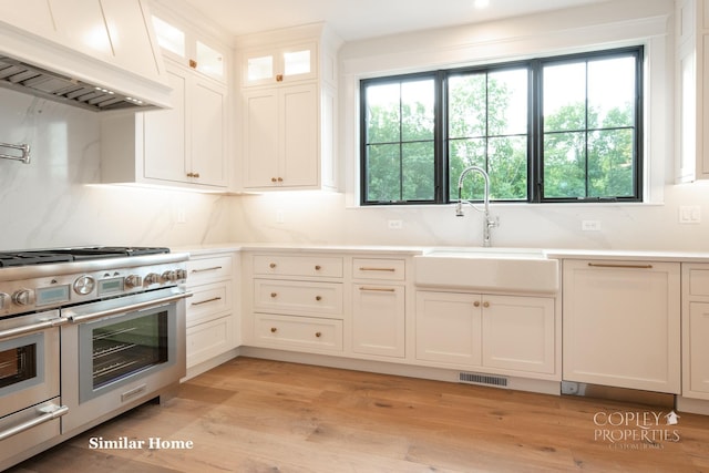 kitchen with sink, light hardwood / wood-style flooring, custom range hood, range with two ovens, and white cabinets