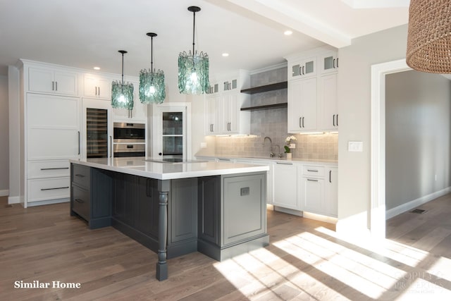 kitchen with hardwood / wood-style floors, tasteful backsplash, sink, white cabinets, and a spacious island