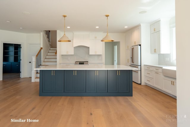 kitchen featuring high quality fridge, a large island, hanging light fixtures, and white cabinets