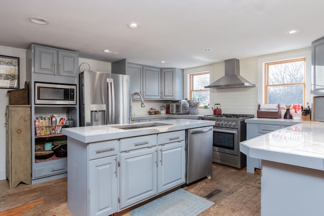 kitchen with sink, hardwood / wood-style flooring, stainless steel appliances, a center island with sink, and wall chimney exhaust hood