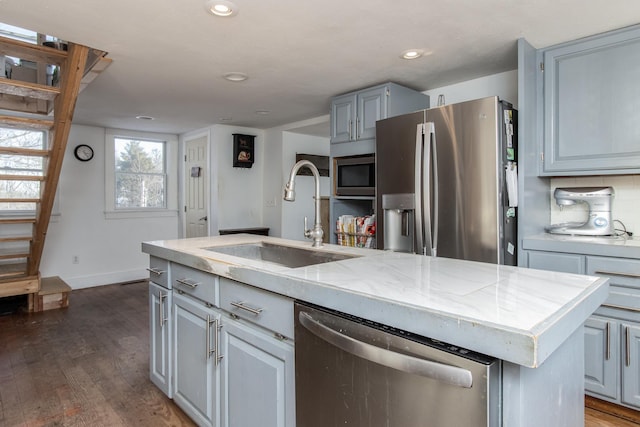 kitchen with sink, gray cabinetry, appliances with stainless steel finishes, dark hardwood / wood-style flooring, and a kitchen island with sink