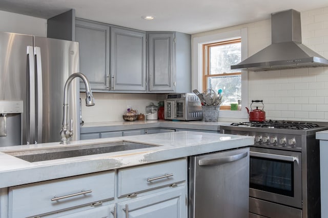 kitchen with sink, gray cabinets, appliances with stainless steel finishes, tasteful backsplash, and wall chimney exhaust hood