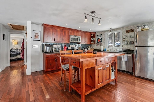 kitchen with dark wood-type flooring, sink, hanging light fixtures, appliances with stainless steel finishes, and decorative backsplash