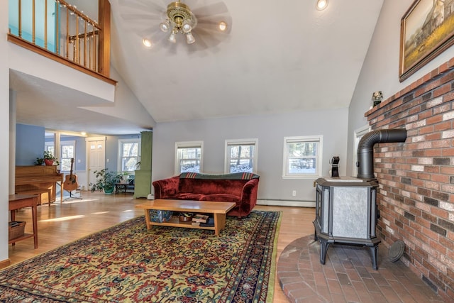 living room with high vaulted ceiling, a wood stove, ceiling fan, light hardwood / wood-style floors, and a baseboard heating unit