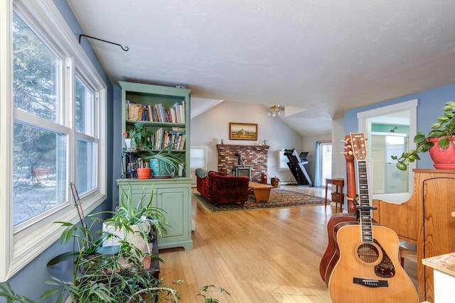 sitting room featuring vaulted ceiling, a wood stove, a wealth of natural light, and light hardwood / wood-style flooring