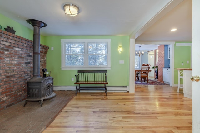 living area featuring a notable chandelier, light hardwood / wood-style floors, baseboard heating, and a wood stove