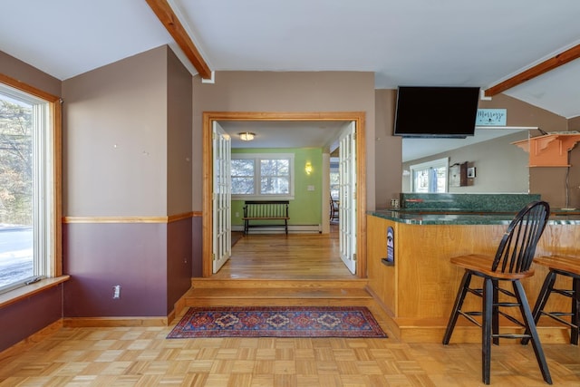 kitchen with lofted ceiling with beams, light parquet floors, a wealth of natural light, and a kitchen breakfast bar