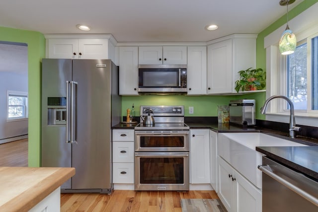 kitchen featuring decorative light fixtures, light hardwood / wood-style floors, white cabinets, and appliances with stainless steel finishes