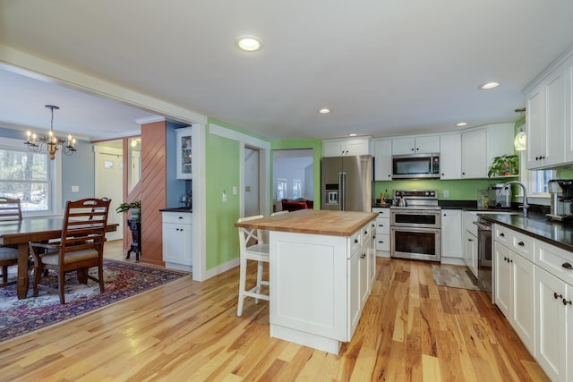 kitchen with pendant lighting, butcher block countertops, appliances with stainless steel finishes, a center island, and white cabinets