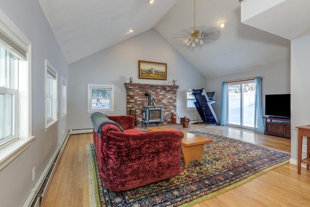 living room with high vaulted ceiling, light wood-type flooring, and a wood stove