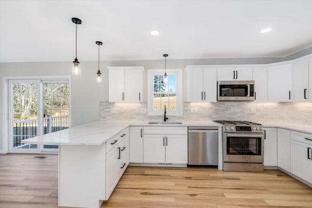 kitchen with appliances with stainless steel finishes, decorative light fixtures, white cabinetry, sink, and kitchen peninsula