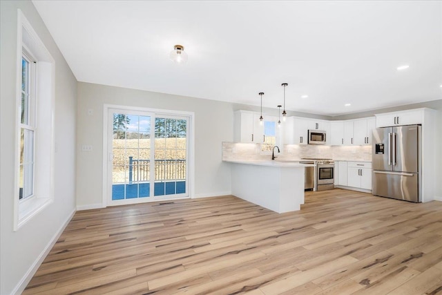 kitchen with hanging light fixtures, stainless steel appliances, white cabinets, decorative backsplash, and kitchen peninsula