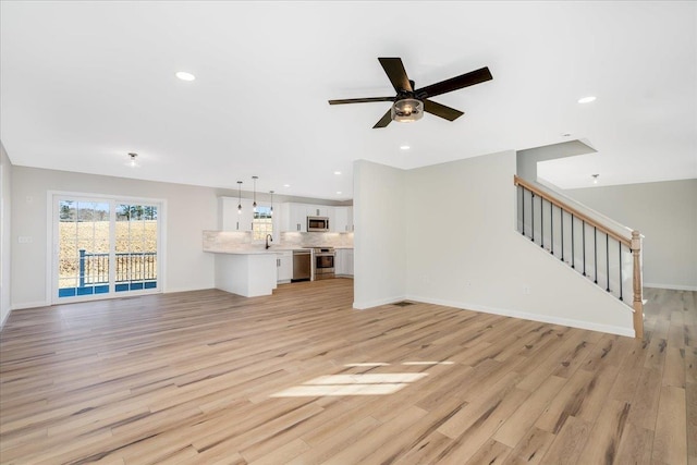 unfurnished living room featuring ceiling fan, sink, and light wood-type flooring