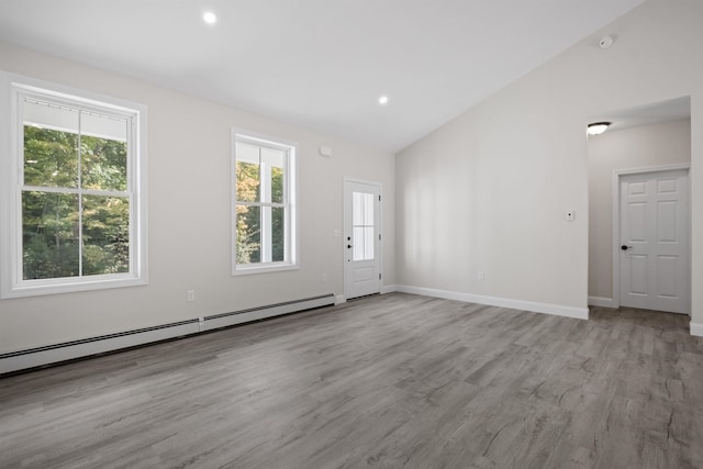 unfurnished room featuring a baseboard radiator, light hardwood / wood-style floors, vaulted ceiling, and a wealth of natural light