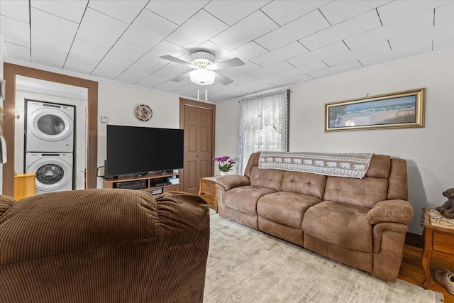 living room featuring light wood-type flooring, ornamental molding, ceiling fan, and stacked washing maching and dryer