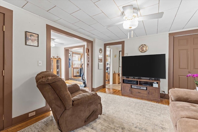 living room with ceiling fan, ornamental molding, and light wood-type flooring