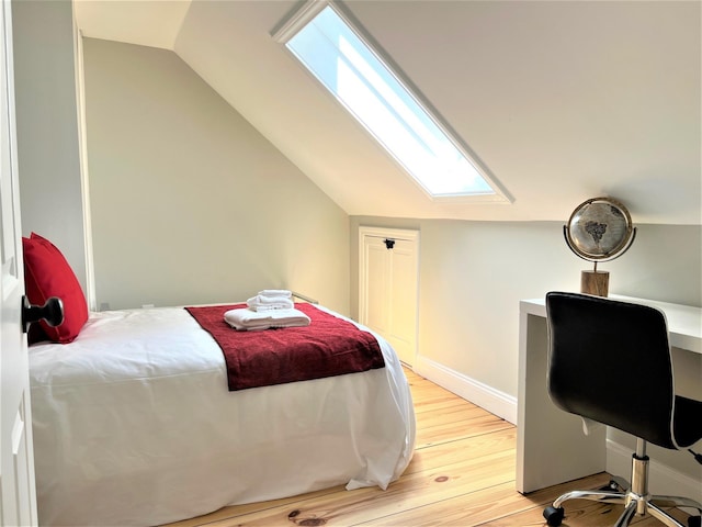 bedroom featuring lofted ceiling with skylight and light hardwood / wood-style flooring