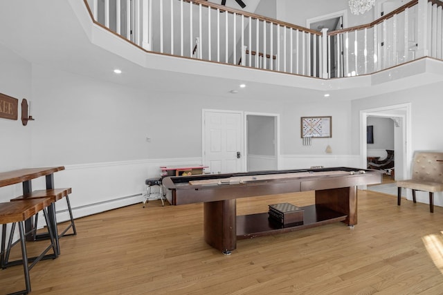 playroom with a towering ceiling, light hardwood / wood-style flooring, and a baseboard heating unit