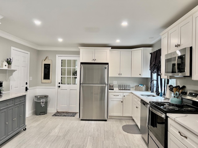 kitchen with sink, appliances with stainless steel finishes, white cabinetry, ornamental molding, and light stone countertops