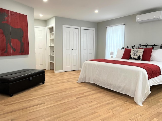 bedroom featuring a wall unit AC, light hardwood / wood-style floors, and multiple closets