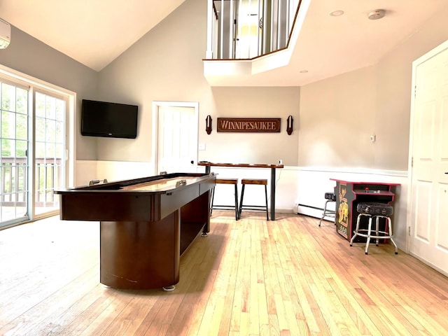 kitchen with a baseboard radiator, high vaulted ceiling, a wall mounted AC, and light hardwood / wood-style floors