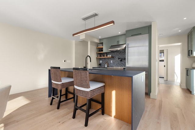 bar featuring built in refrigerator, sink, light wood-type flooring, and decorative backsplash