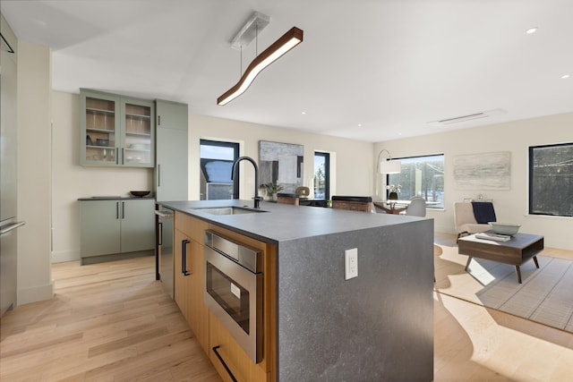 kitchen with a kitchen island with sink, sink, light hardwood / wood-style flooring, and stainless steel microwave