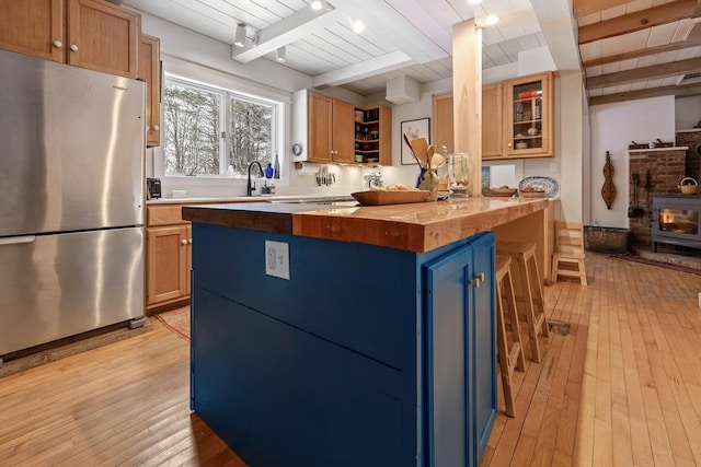 kitchen with light hardwood / wood-style flooring, stainless steel refrigerator, butcher block counters, beam ceiling, and a kitchen bar